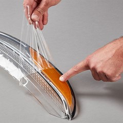 A person removes temporary Surface Protection Film on a vehicle headlight replacement.